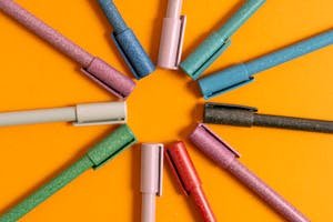A creative arrangement of glittery pens in a circular pattern on an orange background.